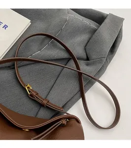 Detail view of adjustable brown leather shoulder strap with golden metal buckle hardware
