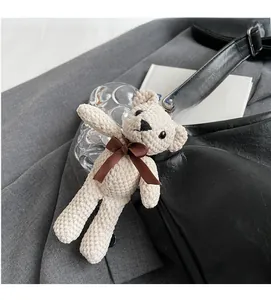 Close-up of a beige woven bear bag charm with brown ribbon on a black leather tote