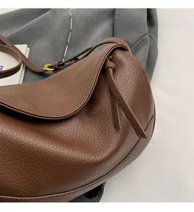 Detail of dark brown leather crossbody bag showing rich litchi grain texture and gold buckle