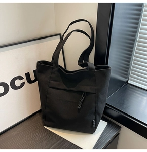 Detalle del bolso tote de lona negra con bolsillo de cremallera y etiqueta tejida