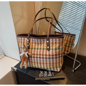 Detail of multi-color houndstooth tote bag featuring plush rabbit charm and brown leather handles
