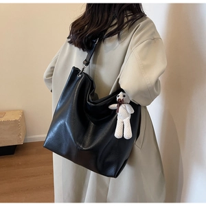 Detail of black tote bag in PU leather with cute white knitted bear charm and metal buckle