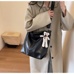 Detail of black leather tote bag with plush bear charm worn with a stylish trench coat