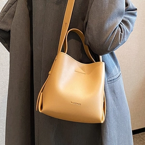Borsa a secchiello color cammello con manico e tracolla regolabile indossata da una modella