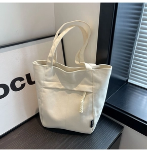 Detalle de un bolso tote de lona crema con bolsillo frontal y colgante de cuerda trenzada