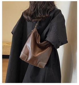 Détail du sac seau en cuir marron foncé avec coutures blanches contrastées sur mannequin