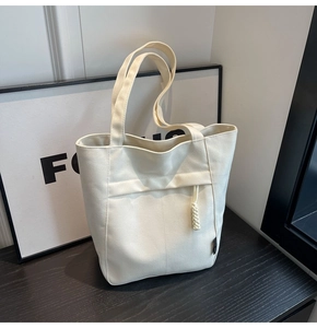 Detalle del bolso tote de lona crema que muestra el bolsillo frontal y el adorno de cuerda