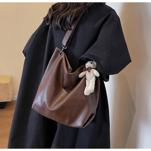 Detail of deep brown leather tote bag featuring a cute cream knitted bear charm