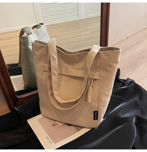 Detalle del bolso tote de lona crema con textura tejida y etiqueta de marca sobre seda negra