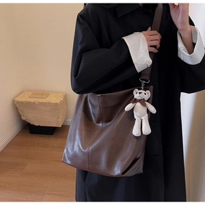 Detail of a large brown leather tote bag with a cute bear pendant on a shoulder strap