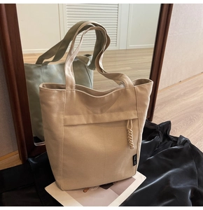 Detalle de bolso tote de lona beige con bolsillo lateral y colgante de borla trenzada