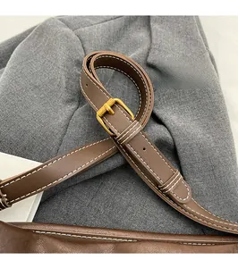 Détail d'une bandoulière en cuir marron avec boucle dorée et surpiqûres blanches de sac seau