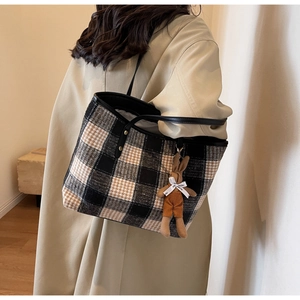 Detailed view of woven plaid tote bag with brown rabbit charm and black leather straps