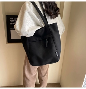 Primer plano de un bolso tote de lona negra con bolsillo frontal y cordón trenzado decorativo