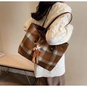 Detail view of brown plaid tote bag with plush rabbit charm and faux leather straps