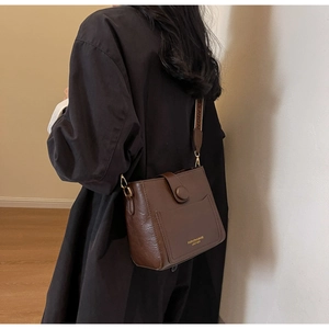 Détail du sac seau en cuir marron foncé avec large bandoulière et lettrage doré chic