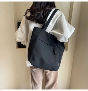 Detalle del bolso tote de lona negra con etiqueta lateral y colgante decorativo anudado