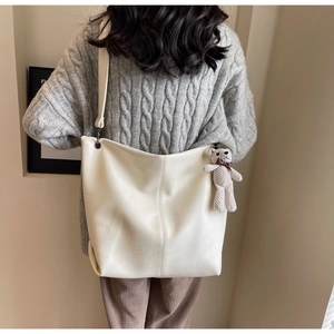 Rear view of model wearing a large cream tote bag with cute bear charm detail