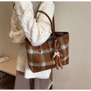 Detail of plaid tote bag with brown leather handles and a plush rabbit charm
