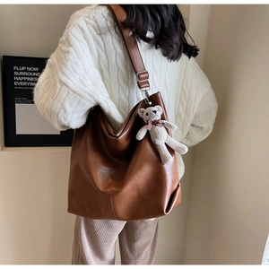 Detail of brown faux leather tote bag featuring a cute beige bear charm and long strap