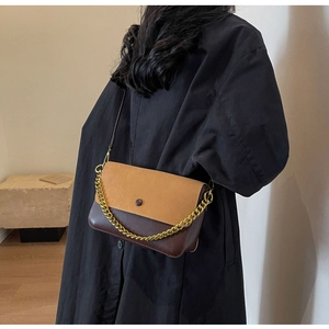 Detail of bicolored vintage leather handbag with golden chain strap on a black coat
