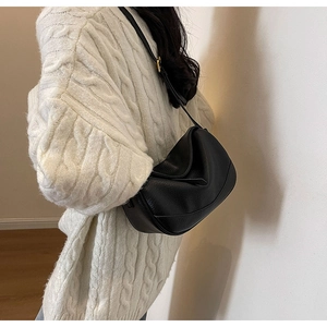 Detail view of black textured leather crescent bag styled with a white knit sweater