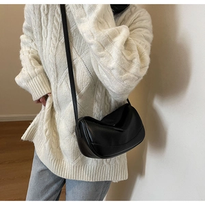 Side view of black lychee-textured leather crescent bag worn over a knit sweater