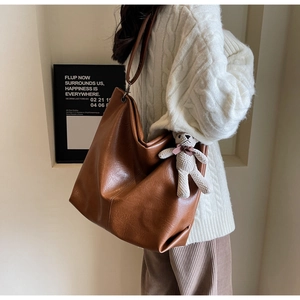 Brown faux leather tote bag with plush bear charm styled on a white knit sweater