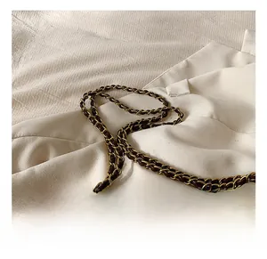 Detail of golden metal chain interwoven with dark brown leather strap on tote bag