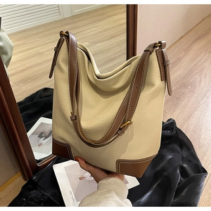 Détail des coutures contrastées et des coins en cuir marron sur un sac seau blanc