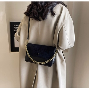 Detail of black crossbody bag with gold chain strap on beige trench coat outfit