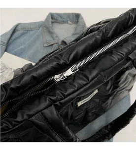 Close-up of a smooth silver zipper on a black quilted puffy tote bag with textile tag