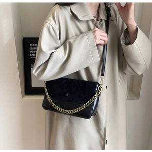 Detail of black crossbody bag with gold chain strap on beige trench coat model