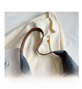 Close-up of blue denim tote bag with brown leather handles and stitched trim detail