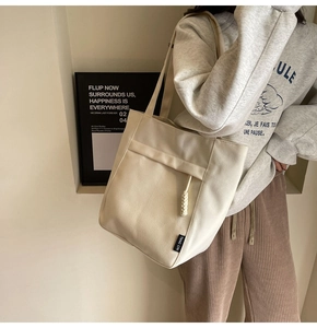Detalle del bolso tote de lona blanco crema con bolsillo frontal y dije de cuerda trenzada