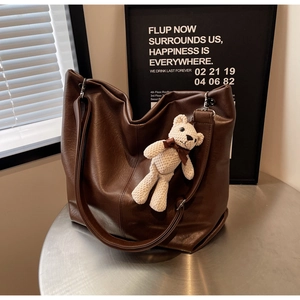 Detail of a brown leather hobo bag with adjustable strap and cute teddy bear pendant
