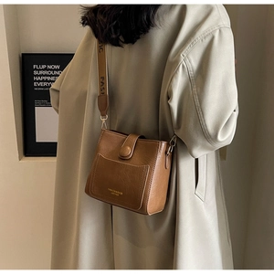 Vue détaillée du sac seau en cuir marron avec large bandoulière et lettrage tendance