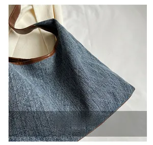 Detailed close-up of blue denim tote bag with white quilted stitching and brown leather trim