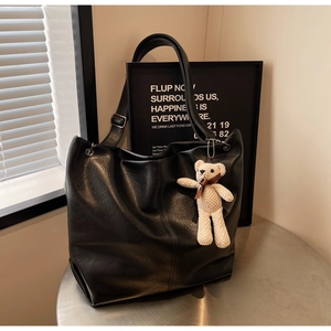 Detail of black tote bag with adjustable strap and cute cream woven bear charm accessory