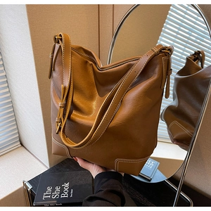 Détail d'un sac seau en cuir marron avec surpiqûres blanches et bandoulière à nœud