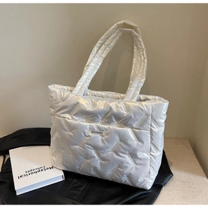 Detailed view of white quilted tote bag with glossy finish and logo label on black leather