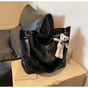 Detail of black faux leather tote bag with stitch decor and cute cream knitted bear charm