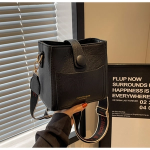 Détail du sac seau en cuir noir avec large bandoulière en toile et lettrage fashion