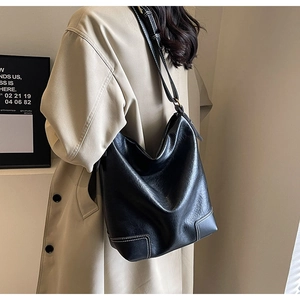 Détail du sac seau en cuir noir avec surpiqûres blanches et large bandoulière