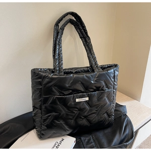 Detail of black quilted puffer tote bag with glossy nylon finish and logo patch