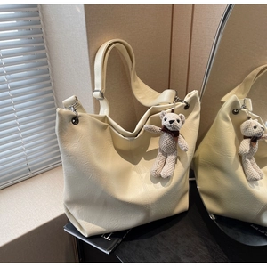 Detail of cream white tote bag with faux leather texture and a cute bear bag charm