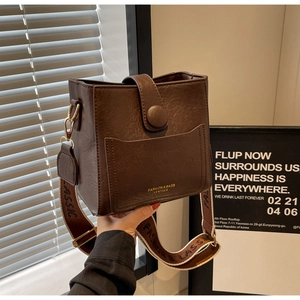 Détail d'un sac seau en cuir marron foncé avec large bandoulière et crochets dorés