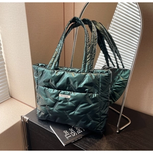 Detail of dark green quilted tote bag with fashion label and plush padded texture
