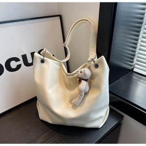 Detailed view of cream-white tote bag with litchi texture and a crochet bear pendant