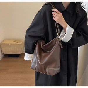 Détail du sac seau en cuir marron foncé avec surpiqûres blanches et boucle dorée de luxe